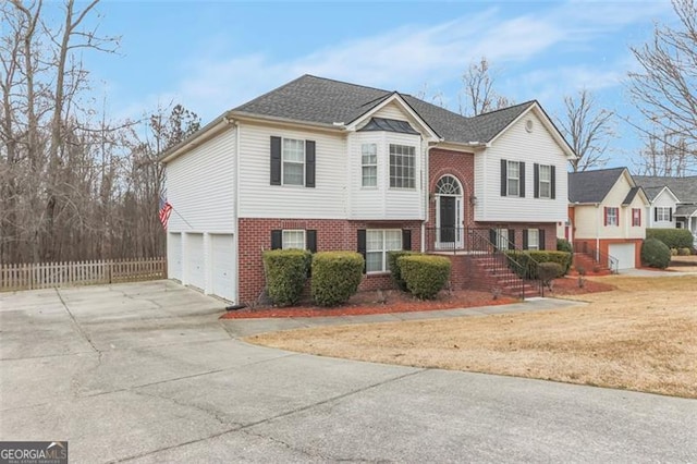 bi-level home with an attached garage, fence, concrete driveway, and brick siding