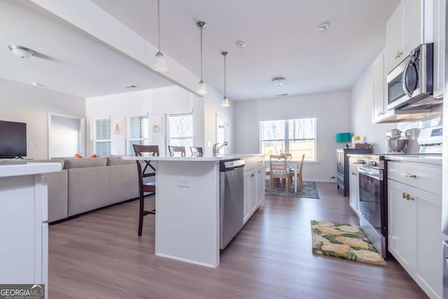 kitchen with dark wood-style floors, appliances with stainless steel finishes, open floor plan, white cabinets, and a kitchen breakfast bar