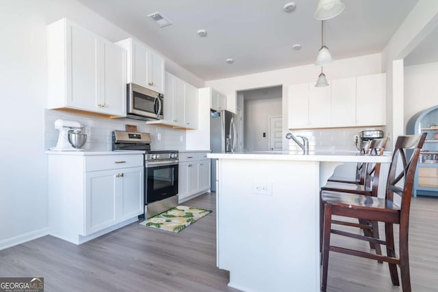 kitchen with visible vents, appliances with stainless steel finishes, wood finished floors, and a breakfast bar