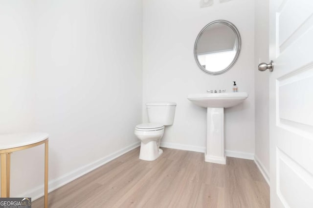 bathroom featuring toilet, a sink, baseboards, and wood finished floors