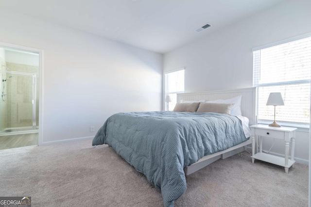 carpeted bedroom featuring ensuite bath, visible vents, and baseboards