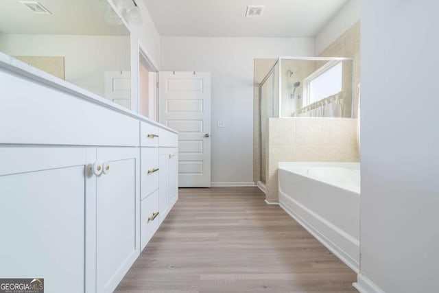 bathroom with wood finished floors, a garden tub, visible vents, and a shower stall