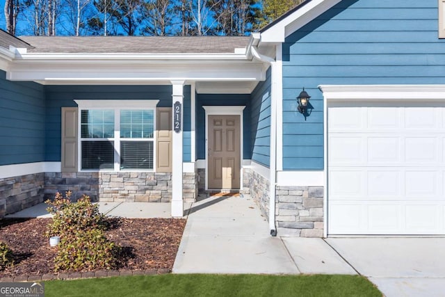 doorway to property with covered porch, stone siding, a shingled roof, and an attached garage