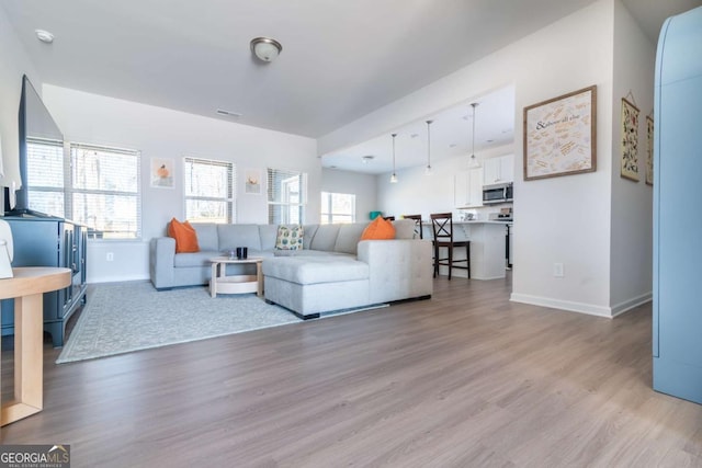 living room with visible vents, light wood-style flooring, and baseboards