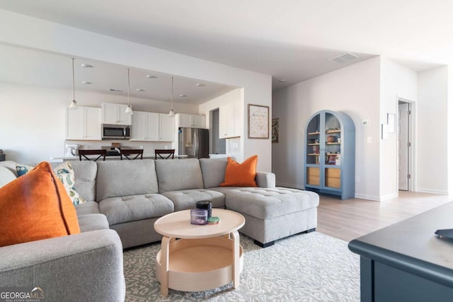 living area with light wood-style flooring, visible vents, arched walkways, and baseboards