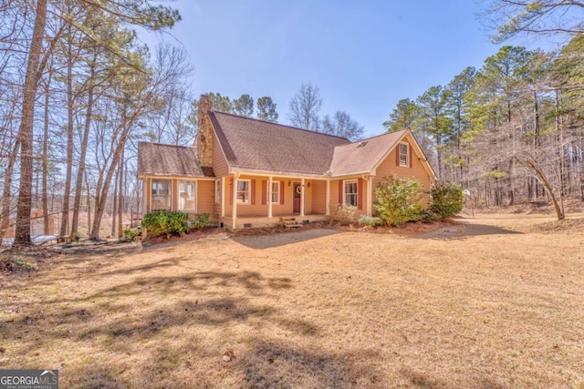 view of front of home featuring a front yard, covered porch, roof with shingles, and a chimney