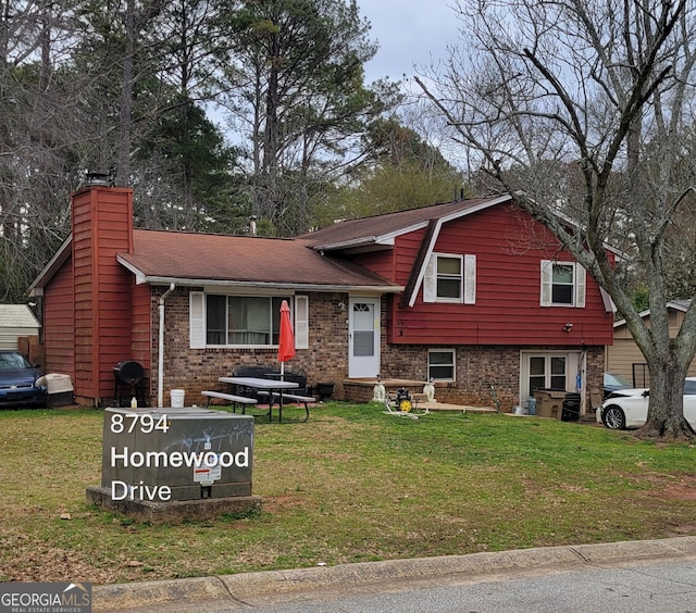 split level home with brick siding, a shingled roof, a gambrel roof, a chimney, and a front yard