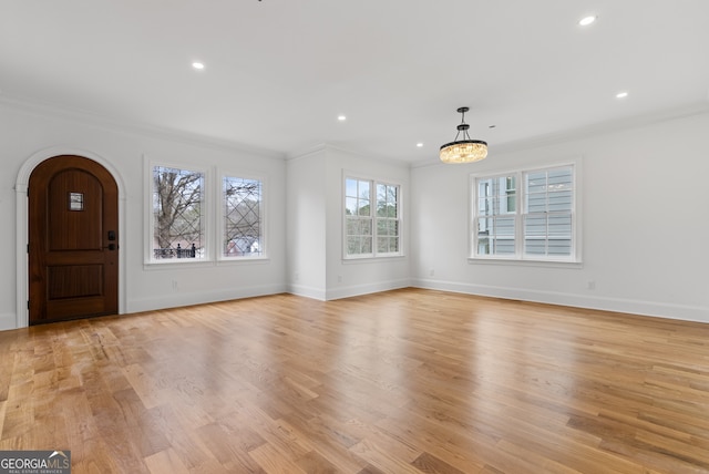 foyer entrance with light wood-type flooring, baseboards, arched walkways, and crown molding