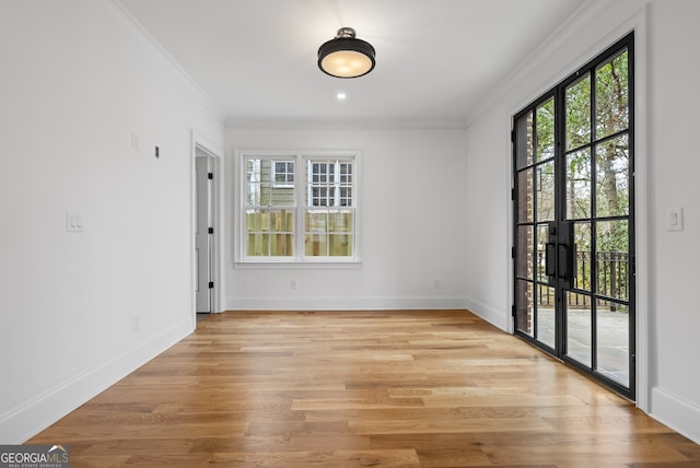 spare room featuring light wood-type flooring, french doors, crown molding, and baseboards