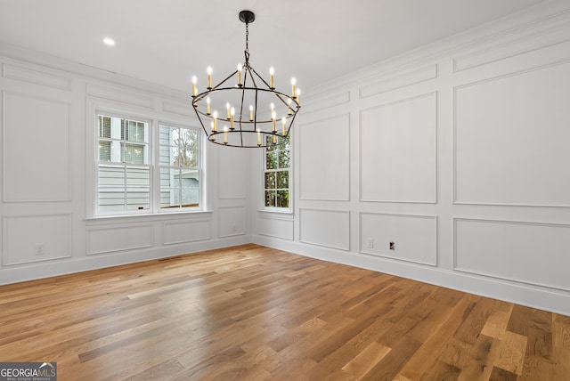 unfurnished dining area with a notable chandelier, crown molding, light wood-style flooring, and a decorative wall