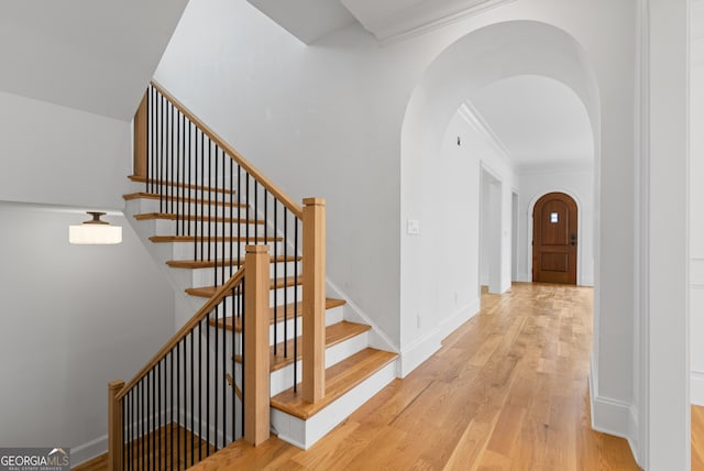 stairs with arched walkways, ornamental molding, wood finished floors, and baseboards