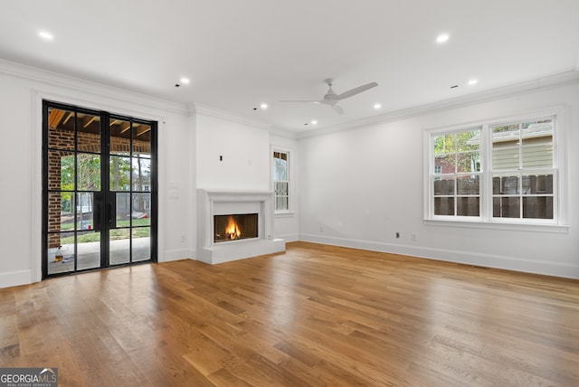 unfurnished living room featuring ornamental molding, a lit fireplace, light wood finished floors, and plenty of natural light