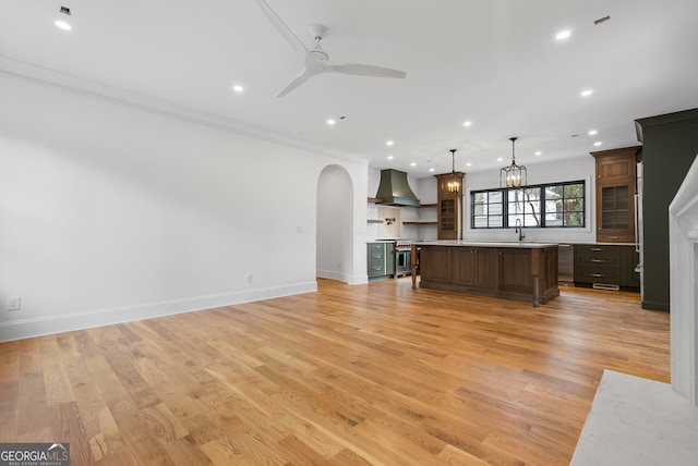 unfurnished living room with arched walkways, ceiling fan, a sink, light wood-style floors, and crown molding