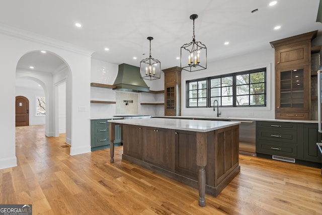 kitchen with arched walkways, wall chimney exhaust hood, light countertops, open shelves, and stainless steel dishwasher