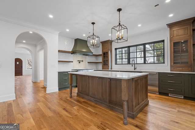 kitchen with a kitchen island, light countertops, wall chimney range hood, open shelves, and stainless steel dishwasher