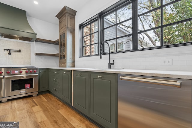 kitchen featuring light wood-style flooring, stainless steel appliances, a sink, wall chimney range hood, and decorative backsplash