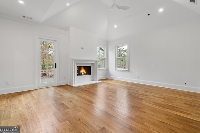 unfurnished living room featuring light wood-type flooring, a warm lit fireplace, ceiling fan, and baseboards