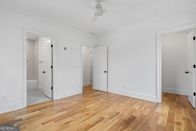 unfurnished bedroom featuring light wood finished floors, a spacious closet, ensuite bathroom, ornamental molding, and baseboards