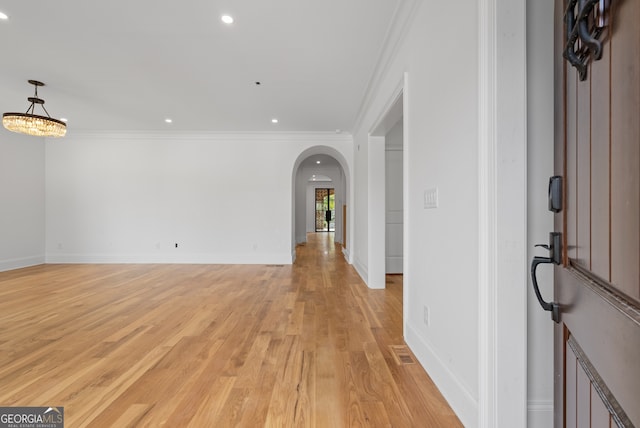 foyer with ornamental molding, arched walkways, light wood-style floors, and baseboards