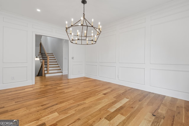 unfurnished dining area with crown molding, light wood finished floors, stairs, and a decorative wall