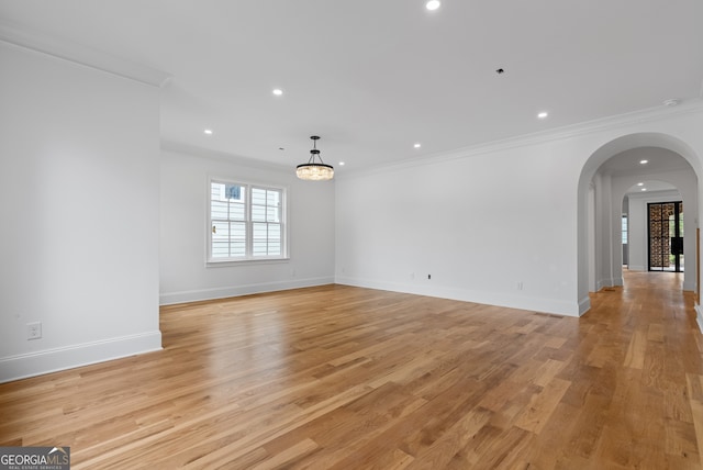 unfurnished room with arched walkways, light wood finished floors, and crown molding