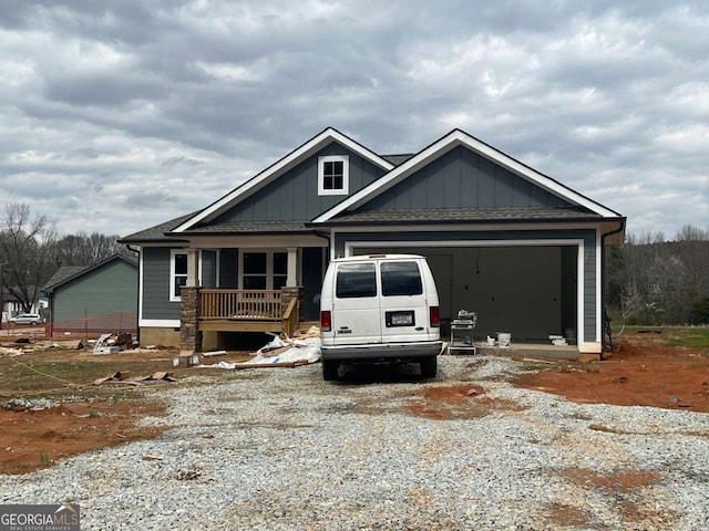 view of front of house featuring gravel driveway, roof with shingles, an attached garage, and covered porch