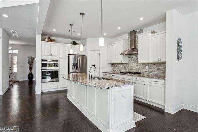 kitchen featuring white cabinets, wall chimney exhaust hood, appliances with stainless steel finishes, dark wood-style flooring, and a sink