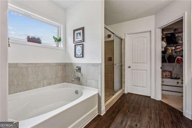 full bathroom featuring a stall shower, a garden tub, a spacious closet, and wood finished floors