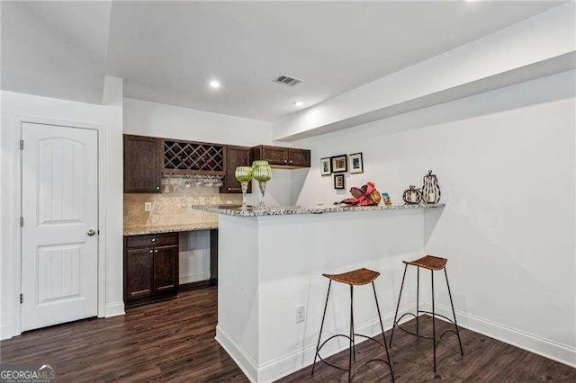 kitchen featuring a peninsula, decorative backsplash, a breakfast bar, and dark brown cabinets