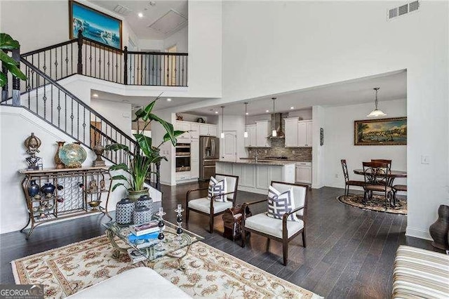 living room with a towering ceiling, visible vents, baseboards, stairway, and dark wood finished floors