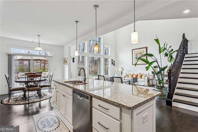 kitchen featuring light stone counters, a sink, white cabinets, stainless steel dishwasher, and dark wood finished floors