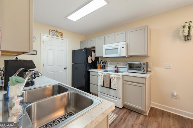 kitchen featuring a toaster, white appliances, wood finished floors, a sink, and light countertops