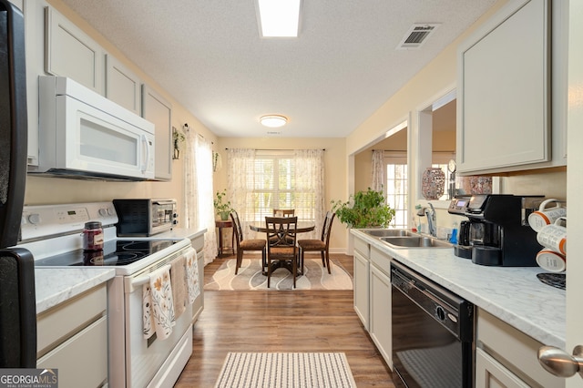 kitchen with white appliances, visible vents, wood finished floors, a textured ceiling, and a sink