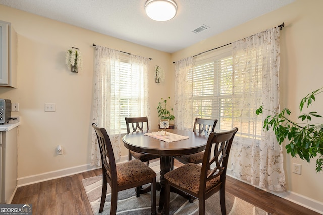 dining area featuring baseboards, a textured ceiling, visible vents, and wood finished floors