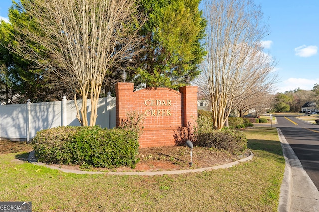 community / neighborhood sign featuring a lawn and fence