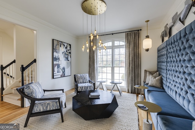 sitting room with ornamental molding, light wood-type flooring, stairway, and an inviting chandelier