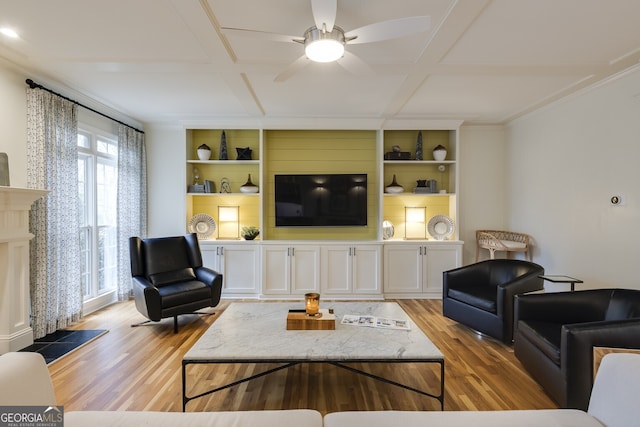 living room with a fireplace with raised hearth, built in shelves, coffered ceiling, and wood finished floors