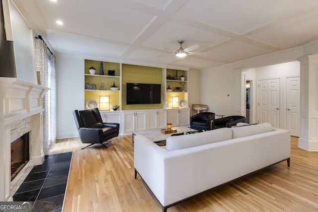 living room featuring light wood-type flooring, coffered ceiling, a fireplace with flush hearth, and decorative columns