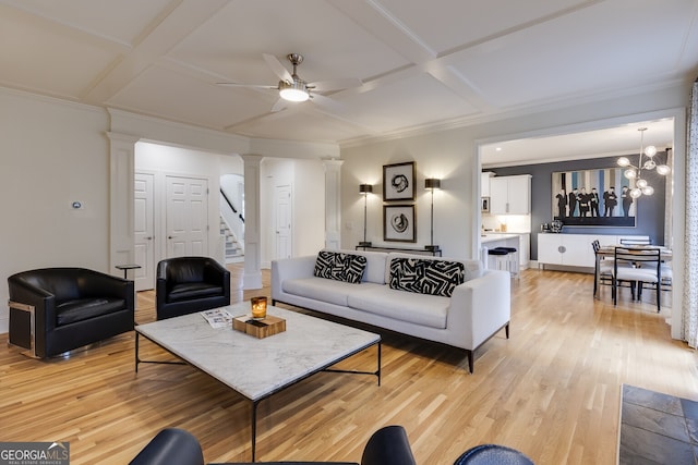 living room featuring ornate columns, coffered ceiling, light wood finished floors, and ceiling fan with notable chandelier