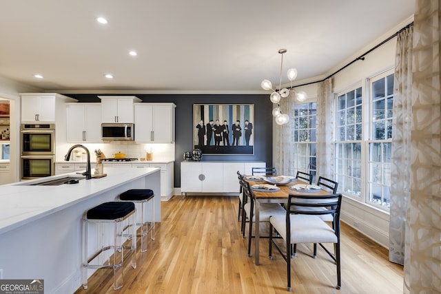 kitchen with white cabinets, light wood-style flooring, appliances with stainless steel finishes, a sink, and backsplash