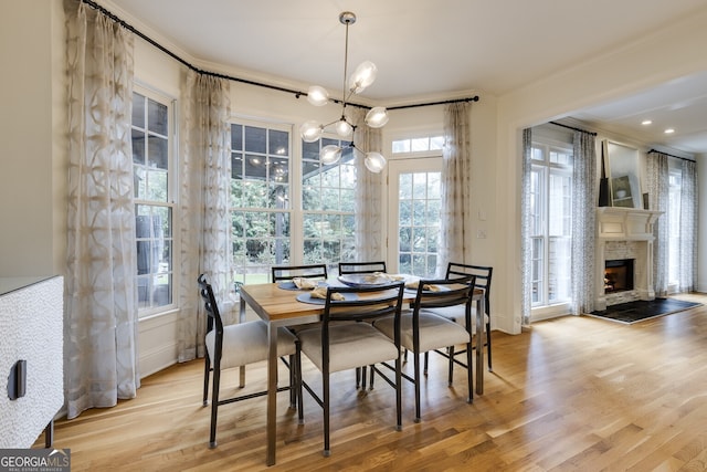 dining area featuring a warm lit fireplace, wood finished floors, and a notable chandelier