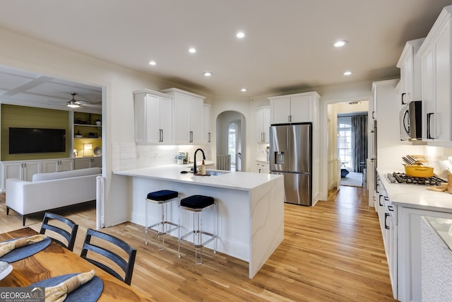 kitchen featuring arched walkways, light wood-style flooring, a peninsula, a sink, and appliances with stainless steel finishes