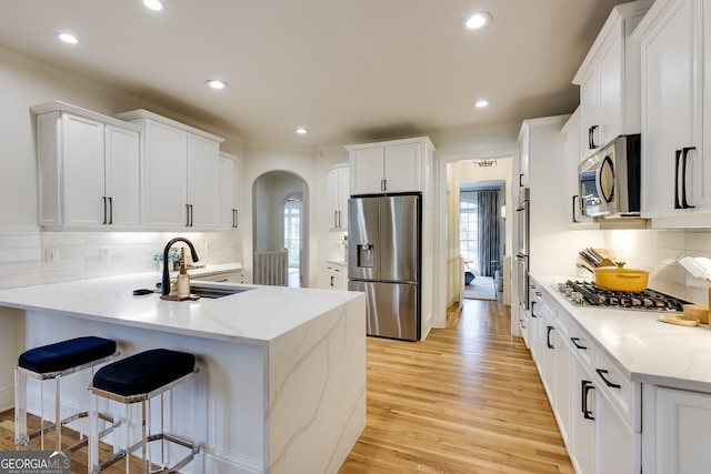 kitchen with arched walkways, light wood-style flooring, a peninsula, stainless steel appliances, and a sink