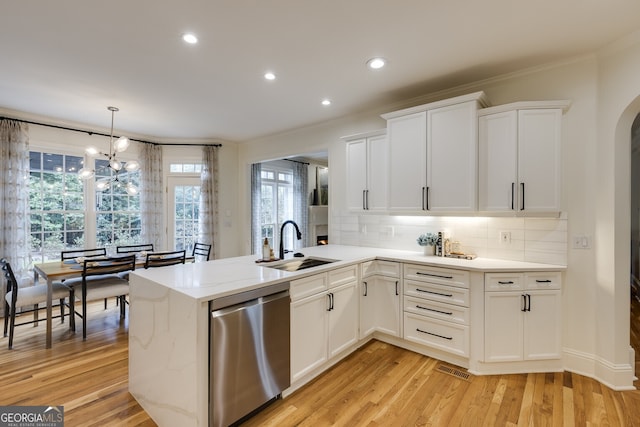 kitchen featuring light wood finished floors, tasteful backsplash, white cabinets, stainless steel dishwasher, and a sink