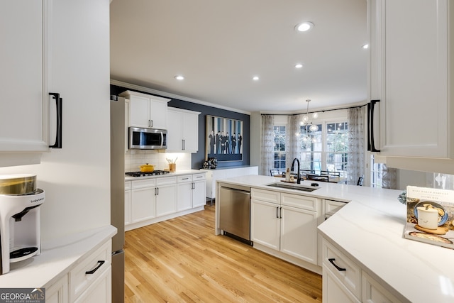 kitchen with light wood-style flooring, a sink, white cabinetry, appliances with stainless steel finishes, and backsplash