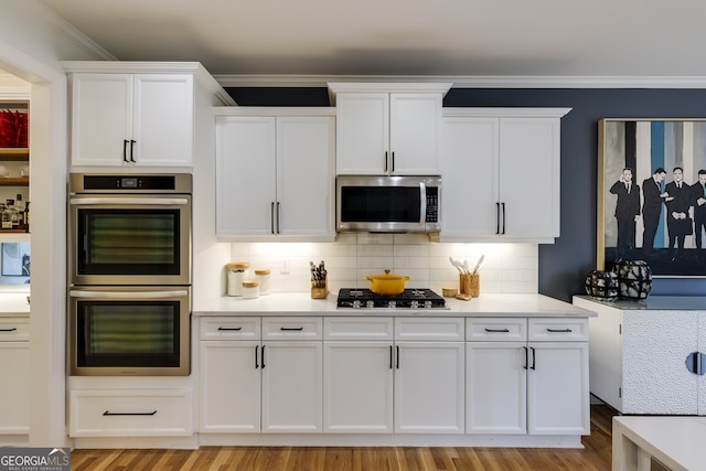 kitchen featuring appliances with stainless steel finishes, white cabinets, light countertops, and ornamental molding