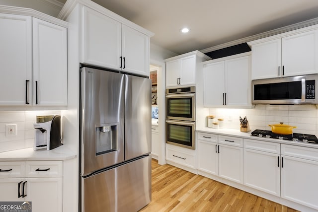 kitchen featuring appliances with stainless steel finishes, decorative backsplash, white cabinetry, and light wood-style floors