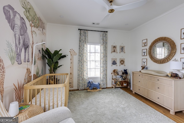 bedroom with visible vents, crown molding, a crib, and wood finished floors