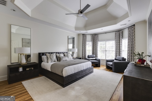 bedroom with a tray ceiling, wood finished floors, and visible vents