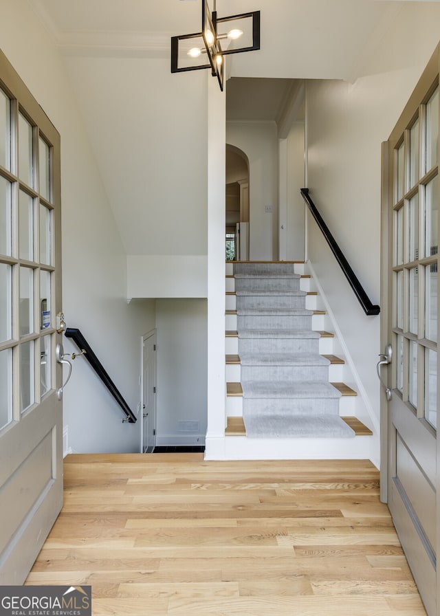 stairs featuring a chandelier, arched walkways, crown molding, and wood finished floors